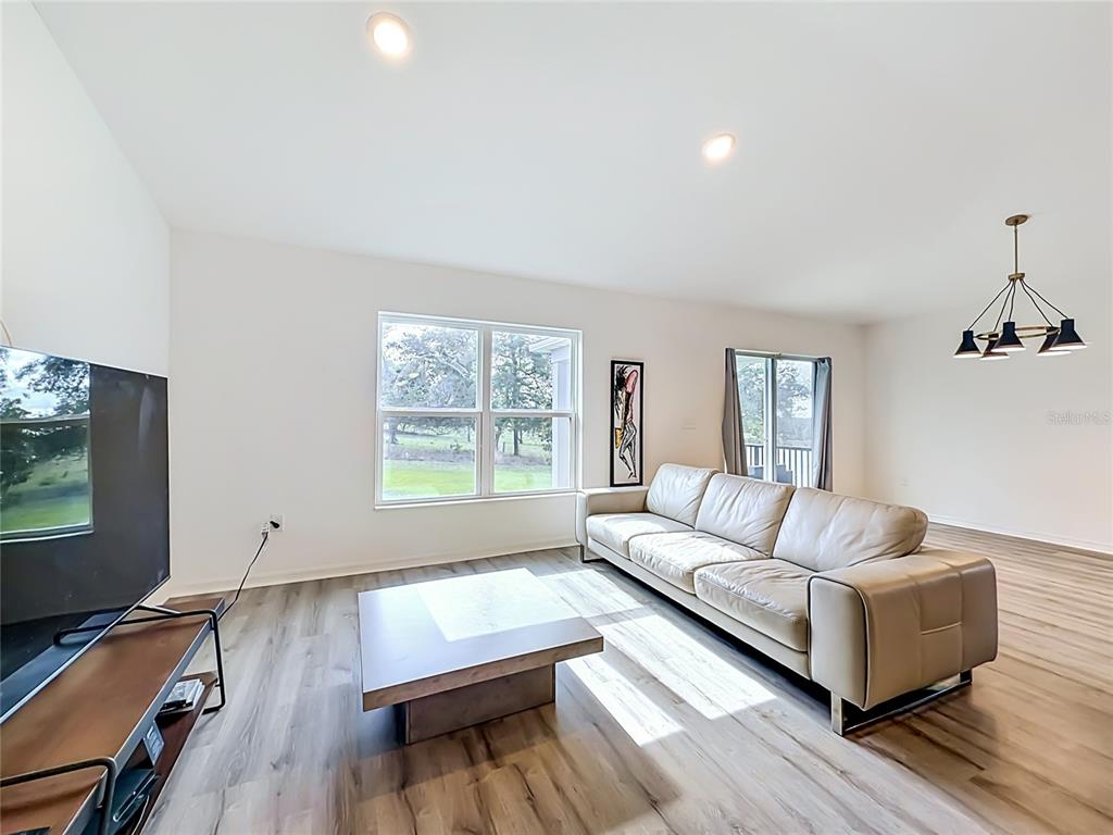 A living room features light wood-look flooring, a beige leather sofa, and a coffee table — 1507 GERANIUM DRIVE, MASCOTTE, FL