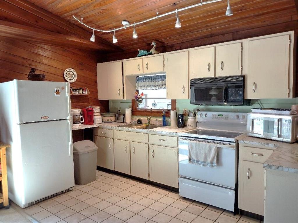 A kitchen with white cabinets, wood-paneled walls, a white refrigerator, and a tiled floor — 1916 LAUREL AVENUE, BUNNELL, FL