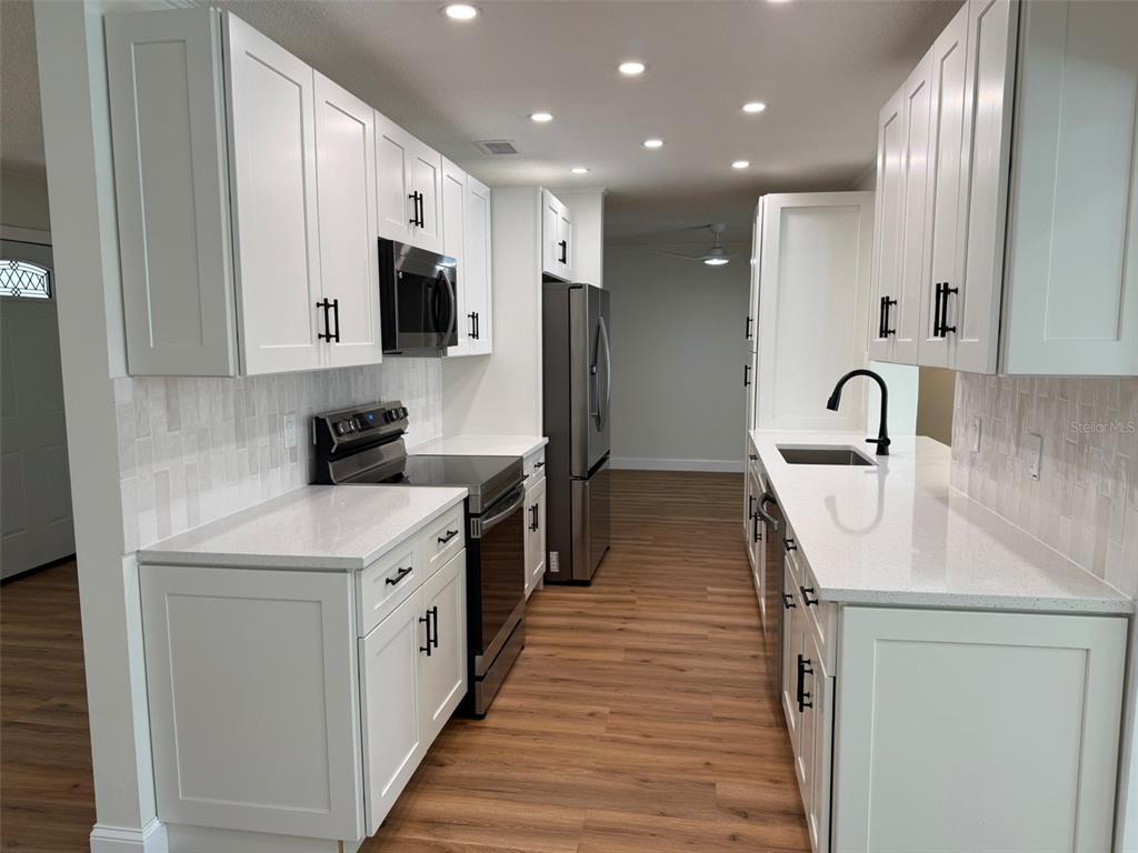 A galley kitchen features white cabinets, stainless steel appliances, quartz countertops, and wood-look flooring — 113 KENDALE DRIVE, SAFETY HARBOR, FL
