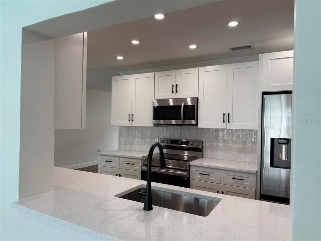 A kitchen features white cabinets, stainless steel appliances, quartz countertops, and a black faucet — 113 KENDALE DRIVE, SAFETY HARBOR, FL