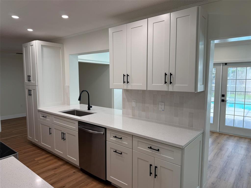 A kitchen features white shaker cabinets, quartz countertops, a stainless steel dishwasher, and wood flooring — 113 KENDALE DRIVE, SAFETY HARBOR, FL
