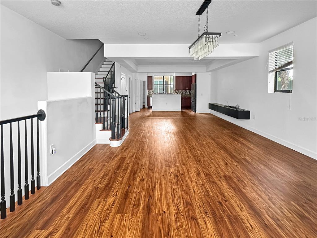 An open-concept living area features wood-look flooring, a staircase with black railings, and a kitchen — 584 COPLEY LANE, ORLANDO, FL