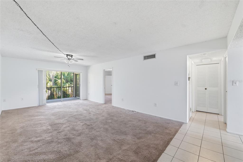 A living room with beige carpet, white walls, a ceiling fan, and a sliding glass door — 130 CYPRESS LANE UNIT 130, OLDSMAR, FL