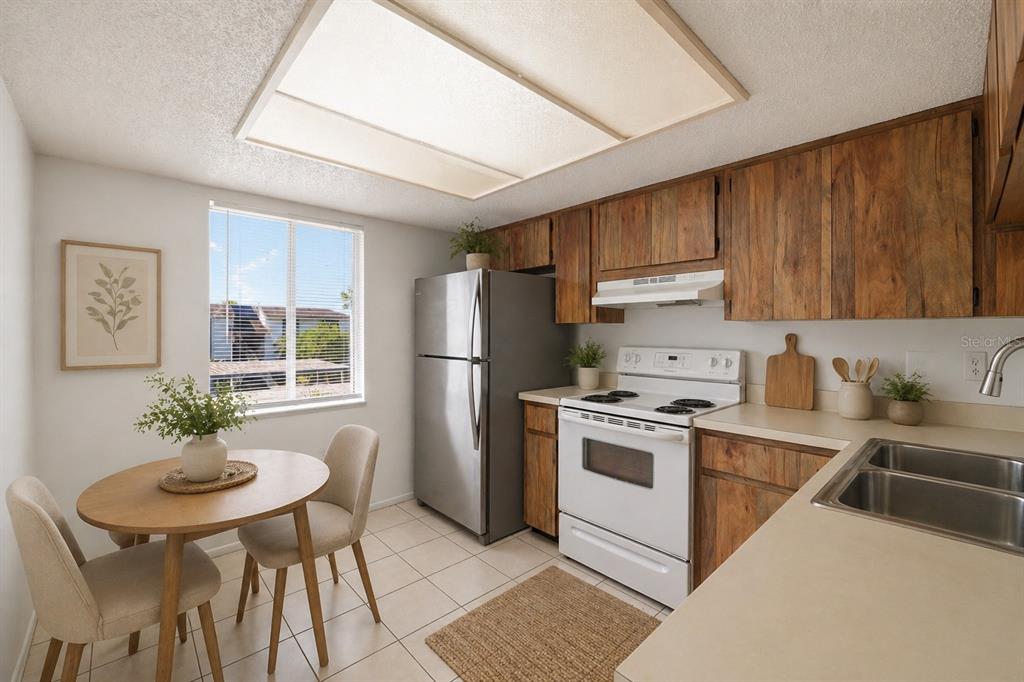 A kitchen features wood cabinets, stainless steel appliances, a dining table, and tile flooring — 130 CYPRESS LANE UNIT 130, OLDSMAR, FL