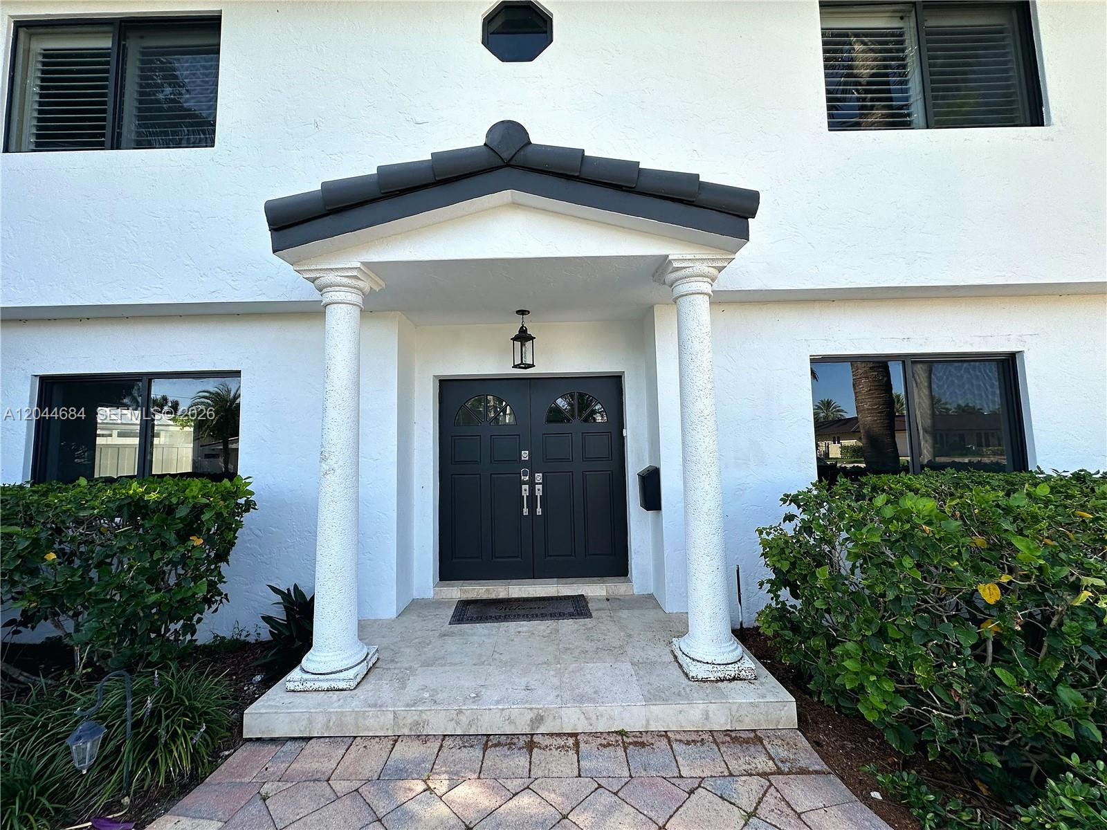 The exterior of a white house features a covered entryway with two columns and black doors — 2445 SE 8th St, Pompano Beach FL 33062, POMPANO BEACH, FL