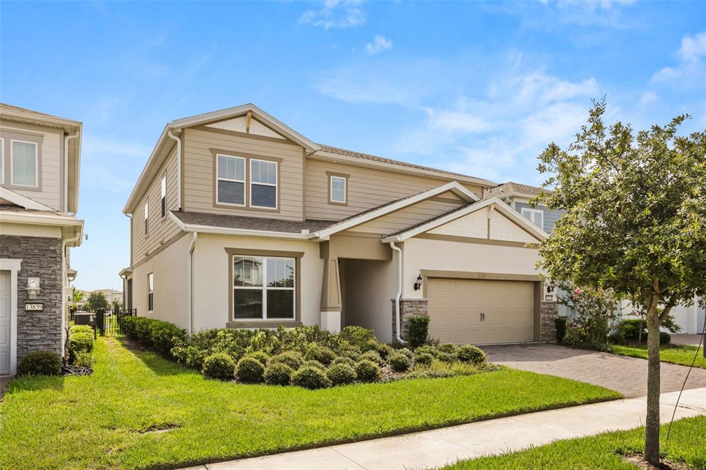 A two-story suburban house with beige siding, a stone-accented garage, and a manicured front lawn — 13865 DESTIN BEACH LANE, ORLANDO, FL
