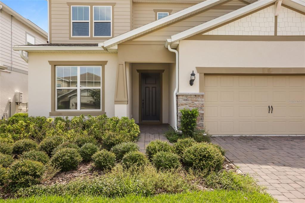 A two-story house exterior features tan siding, a stone accent wall, and a paved driveway — 13865 DESTIN BEACH LANE, ORLANDO, FL