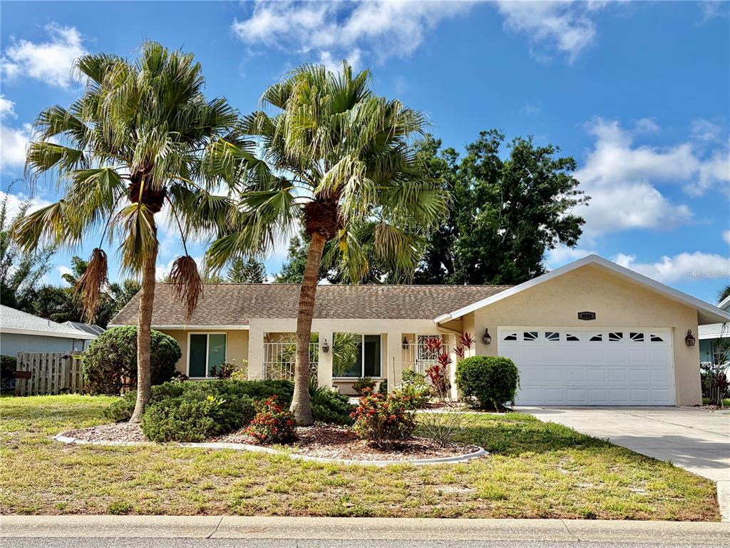 A single-story house with a two-car garage, palm trees, and landscaping under a blue sky — 4892 GREENCROFT ROAD, SARASOTA, FL
