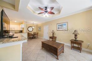 This living room features a tray ceiling with a fan, tile flooring, and a dining area — 2724 VIA MURANO UNIT 630, CLEARWATER, FL