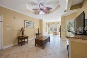A living room features tile flooring, a tray ceiling with a fan, and wooden furniture — 2724 VIA MURANO UNIT 630, CLEARWATER, FL