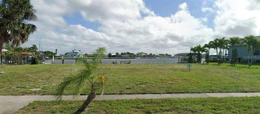 A vacant grassy lot overlooks a canal with boat docks and palm trees under a cloudy sky — 164 MORGAN LANE SE, PORT CHARLOTTE, FL