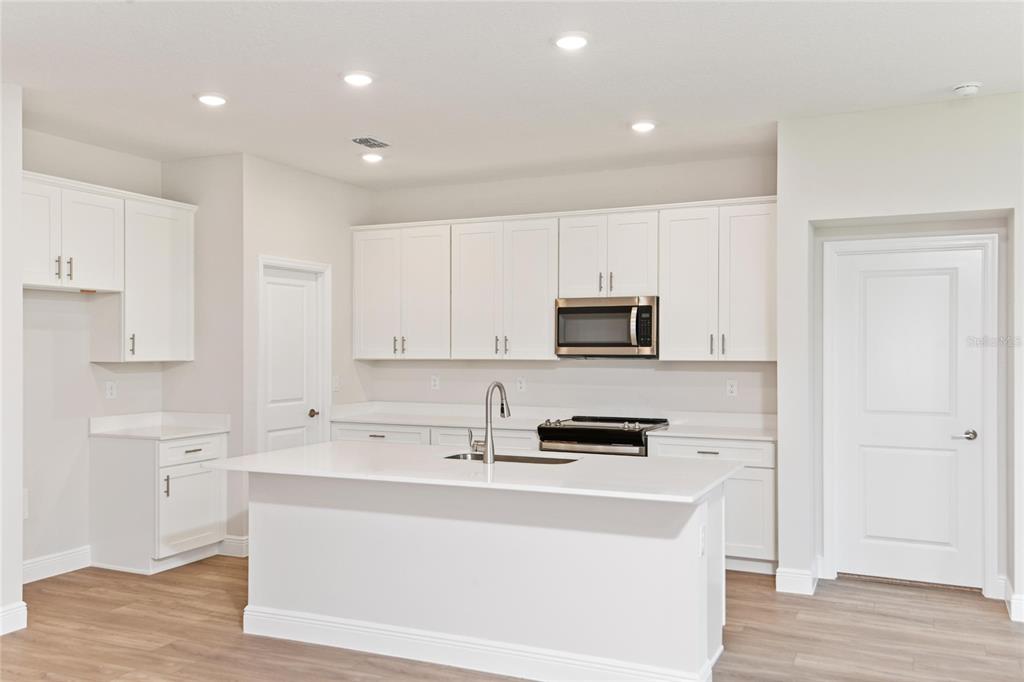 A kitchen with white cabinets, a central island, stainless steel appliances, and light wood flooring — 6225 SW 97TH STREET, OCALA, FL