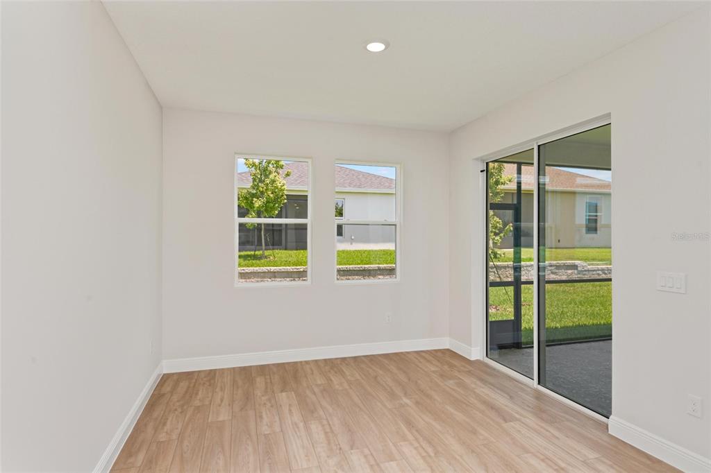 An empty room with light wood-look flooring, two windows, and a sliding glass door — 6225 SW 97TH STREET, OCALA, FL