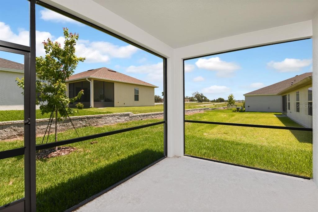 A screened-in concrete patio overlooks a grassy backyard and neighboring houses under a blue sky — 6225 SW 97TH STREET, OCALA, FL