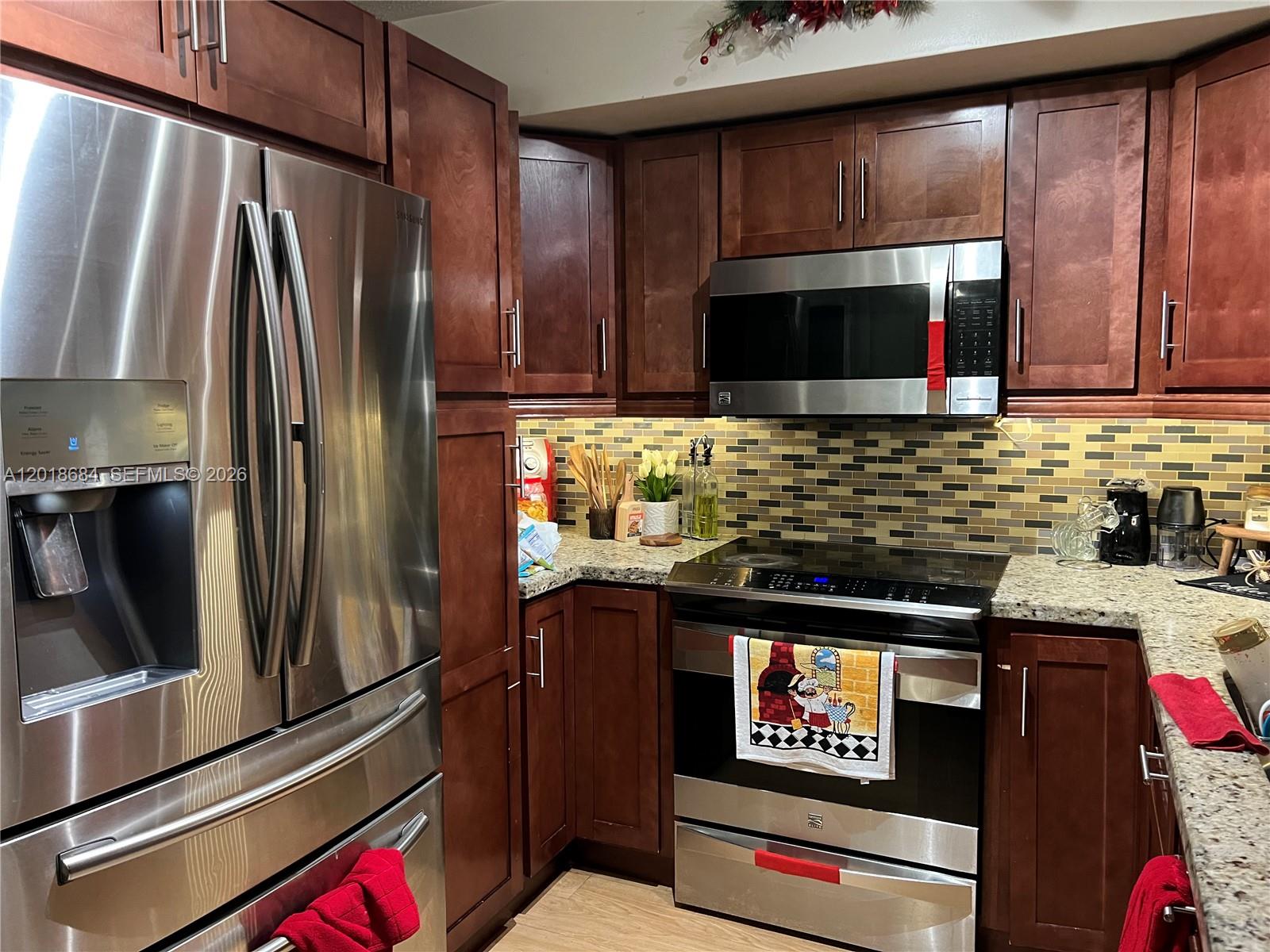 A kitchen features dark wood cabinets, stainless steel appliances, and a mosaic tile backsplash — 2075 SW 122nd Ave # 207, Miami FL 33175, MIAMI, FL