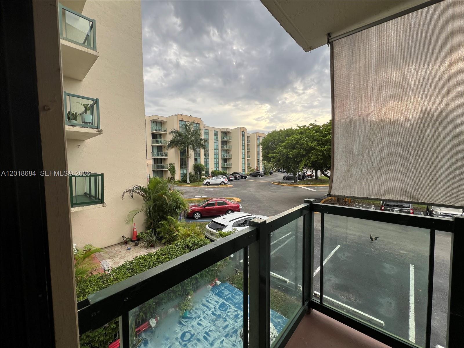 A view from a balcony overlooking a parking lot and apartment buildings under a cloudy sky — 2075 SW 122nd Ave # 207, Miami FL 33175, MIAMI, FL
