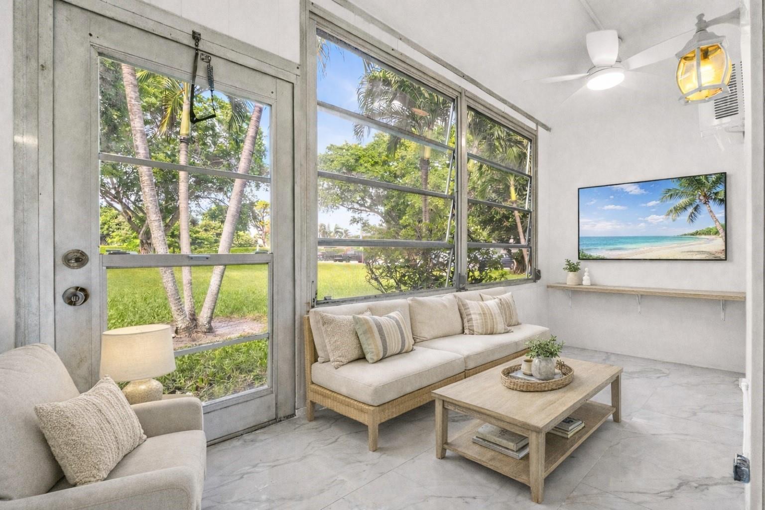 A sunroom features a beige sofa, coffee table, large windows, and a wall-mounted television — 242 Tilford L # L, Deerfield Beach FL 33442, DEERFIELD BEACH, FL
