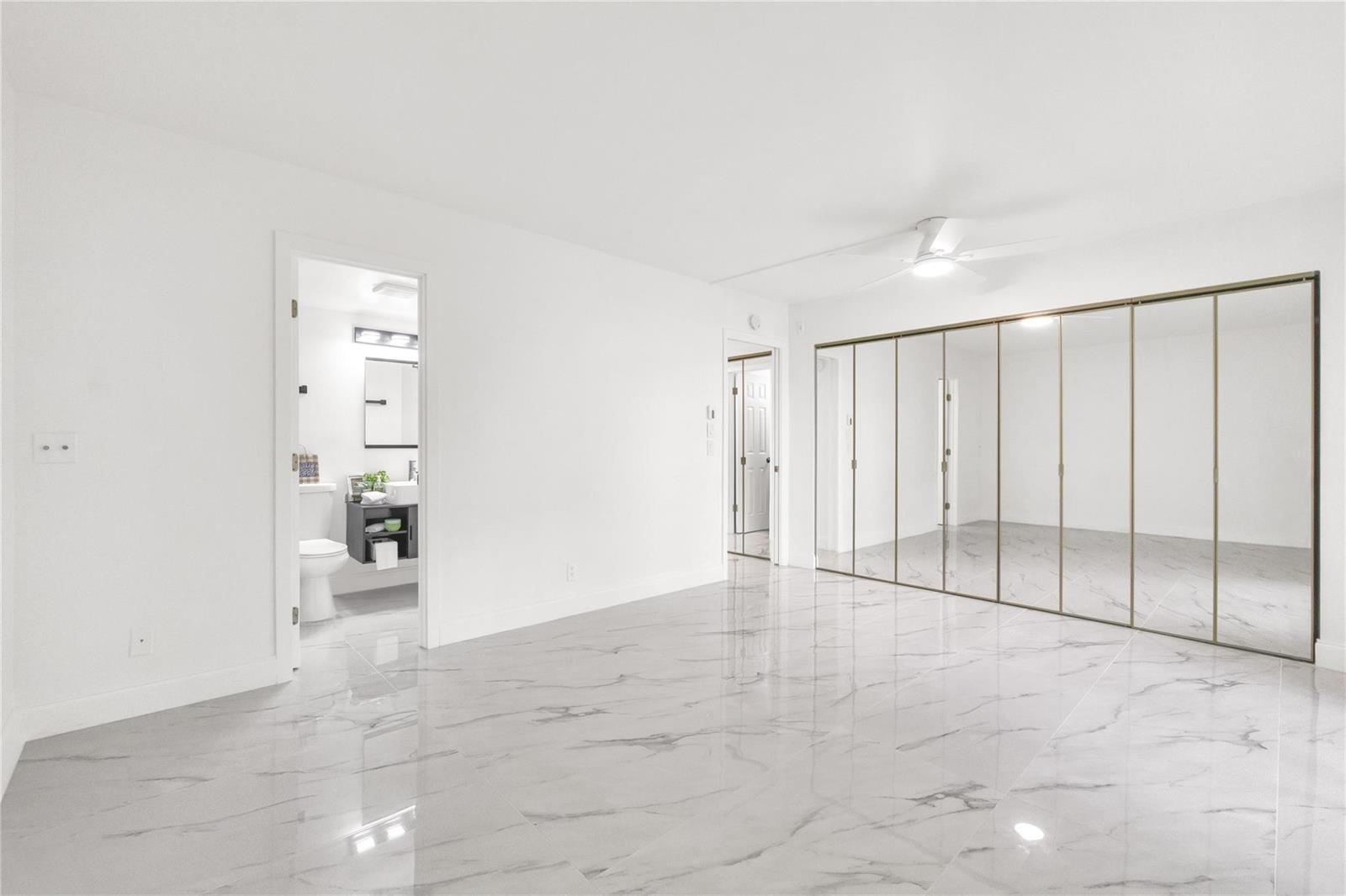 A bedroom with white walls, marble-patterned tile flooring, and a large wall of mirrored closets — 242 Tilford L # L, Deerfield Beach FL 33442, DEERFIELD BEACH, FL