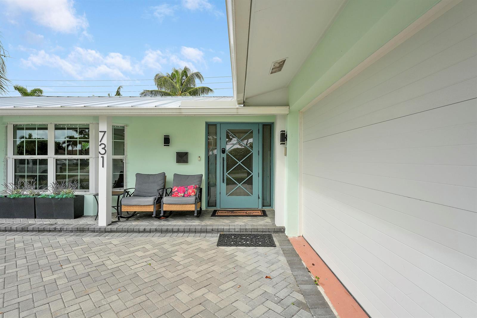 A light green house exterior features a blue front door and a paved driveway — 731 Cruiser Road S, North Palm Beach FL 33408, NORTH PALM BEACH, FL