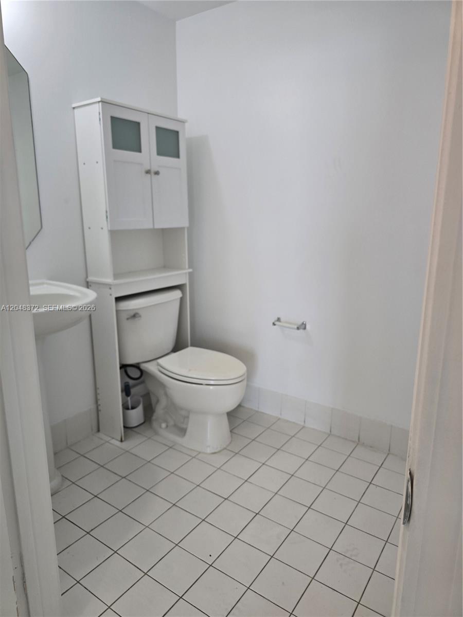 A small bathroom features a pedestal sink, a toilet, and a white over-the-toilet storage cabinet — 117 NW 42nd Ave # 503, Miami FL 33126, MIAMI, FL