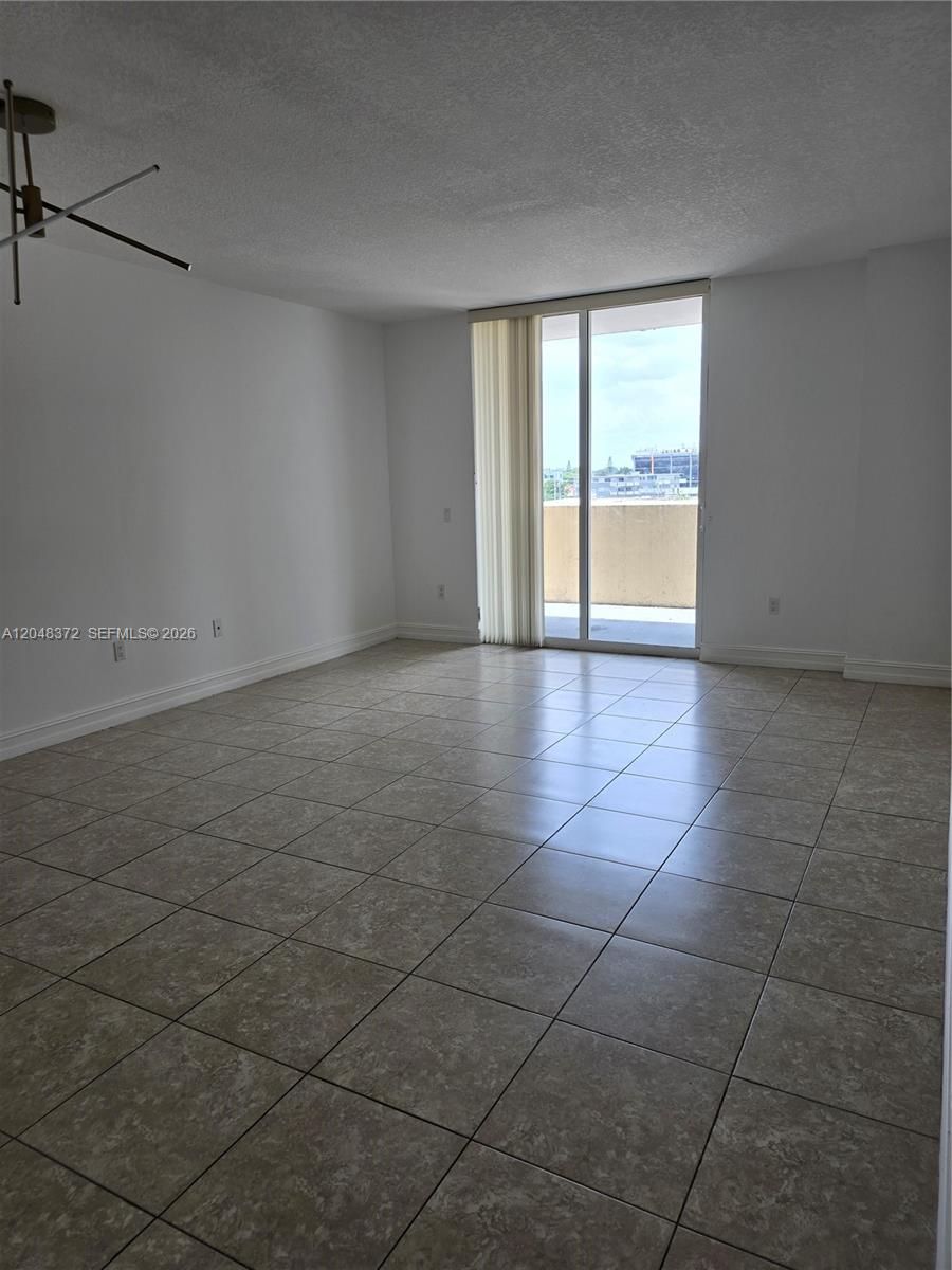 An empty room features beige tile flooring, white walls, and a sliding glass door — 117 NW 42nd Ave # 503, Miami FL 33126, MIAMI, FL