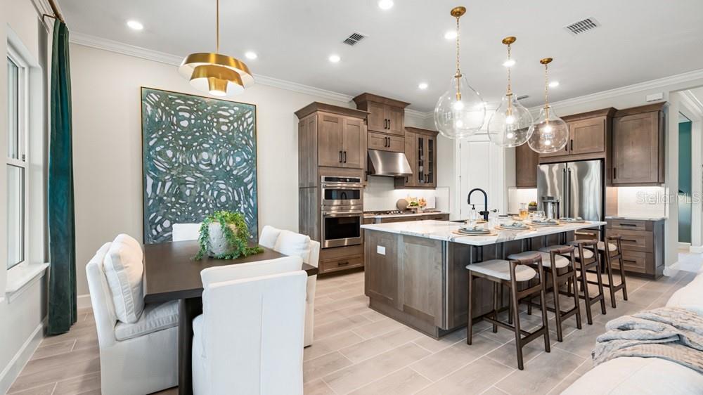 A modern kitchen features wood cabinets, a large island with bar seating, and an adjacent dining area — 10577 ECLIPSE STREET, SARASOTA, FL