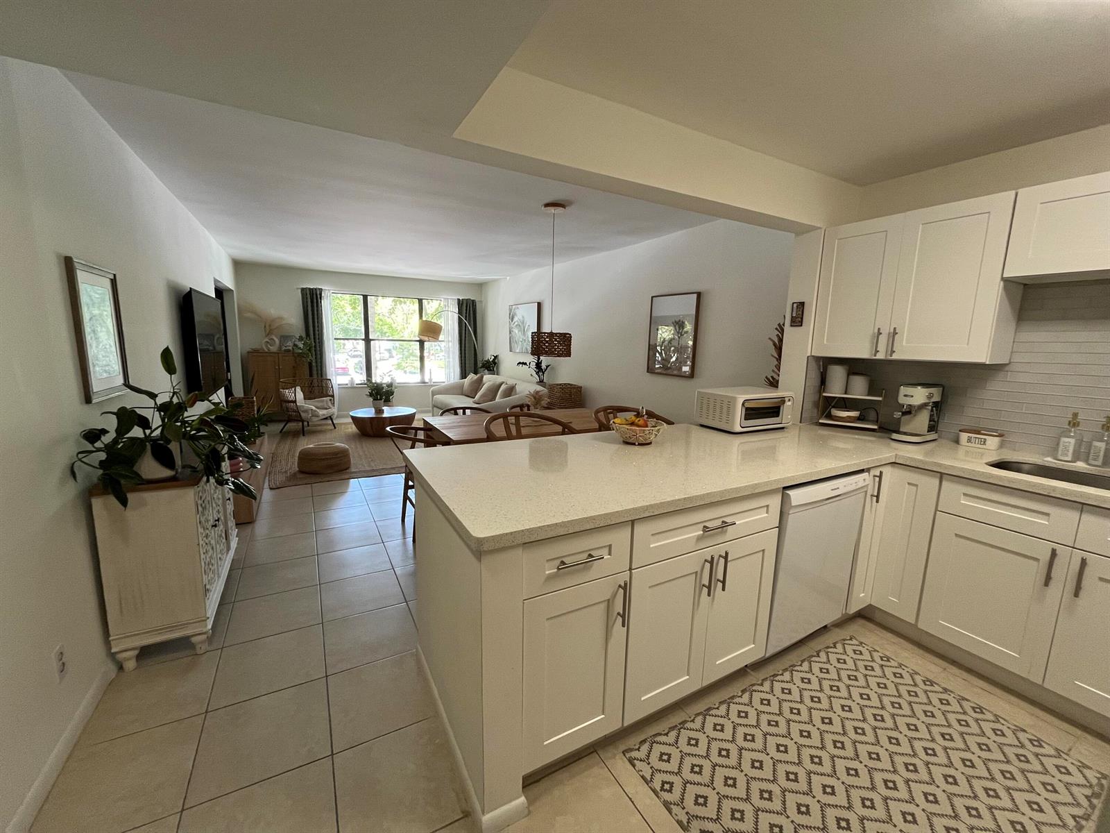 A kitchen with white cabinets and quartz countertops opens into a living and dining area — 2307 S Cypress Bend Drive # 207a, Pompano Beach FL 33069, POMPANO BEACH, FL