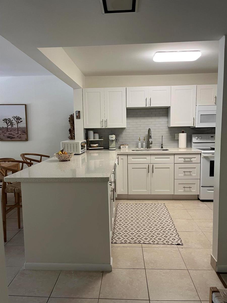 A kitchen features white cabinetry, light-colored countertops, a subway tile backsplash, and tile flooring — 2307 S Cypress Bend Drive # 207a, Pompano Beach FL 33069, POMPANO BEACH, FL