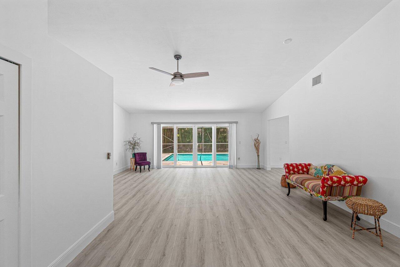 A bright living room features light wood-look flooring, a ceiling fan, and sliding glass doors — 6930 NW 2nd Terrace, Boca Raton FL 33487, BOCA RATON, FL