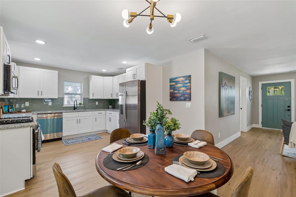 A dining area with a round wooden table sits adjacent to a white kitchen — 5802 12TH AVENUE S, TAMPA, FL