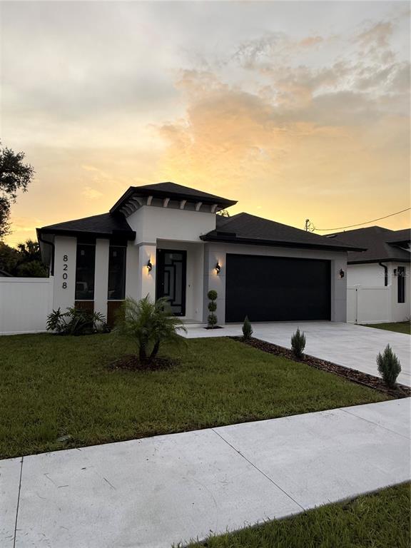 A modern single-story house with a black garage door, white exterior, and a landscaped front yard — 8208 N ELMER STREET, TAMPA, FL