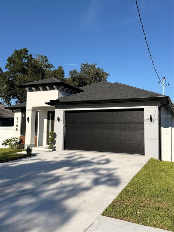 A modern single-story house with a white facade, dark garage door, and gray roof — 8208 N ELMER STREET, TAMPA, FL