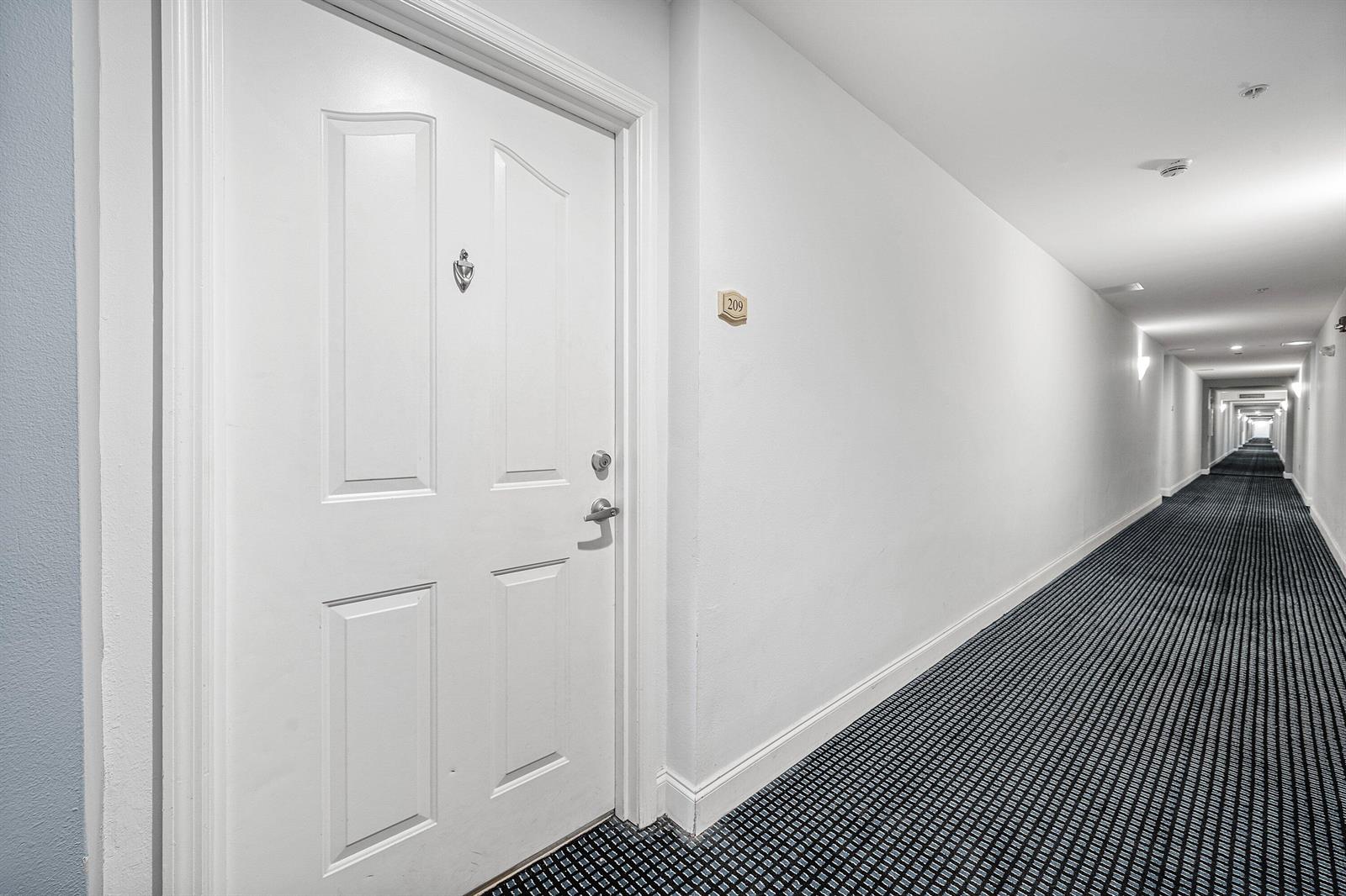 A white door with a number 209 plaque opens into a long, carpeted apartment hallway — 250 NE 3rd Avenue # 1209, Delray Beach FL 33444, DELRAY BEACH, FL