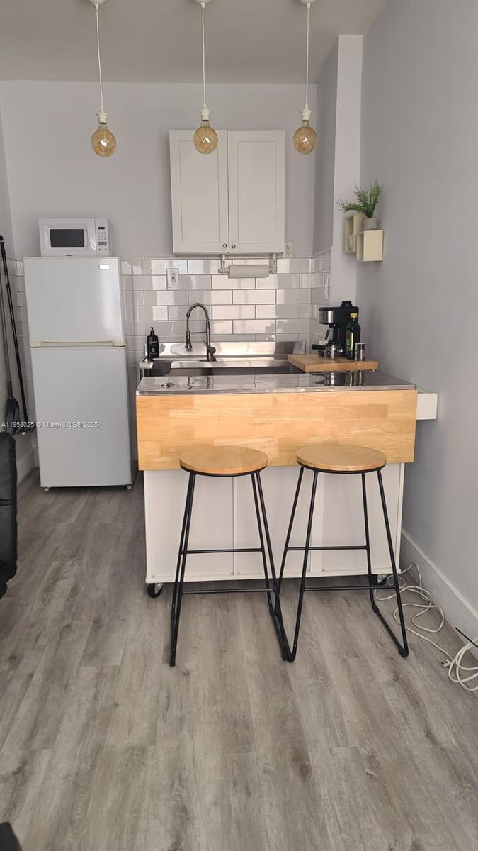 A small kitchen features white cabinets, a stainless steel sink, and a wooden breakfast bar — 3710 Collins Ave # 309, Miami Beach FL 33140, MIAMI BEACH, FL