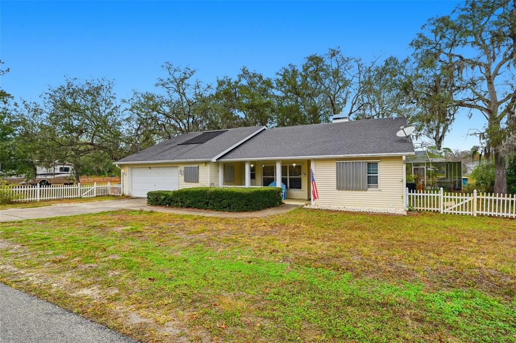A single-story house with a garage, light siding, and a white fence under blue skies — 12227 TERRA CEIA AVENUE, NEW PORT RICHEY, FL