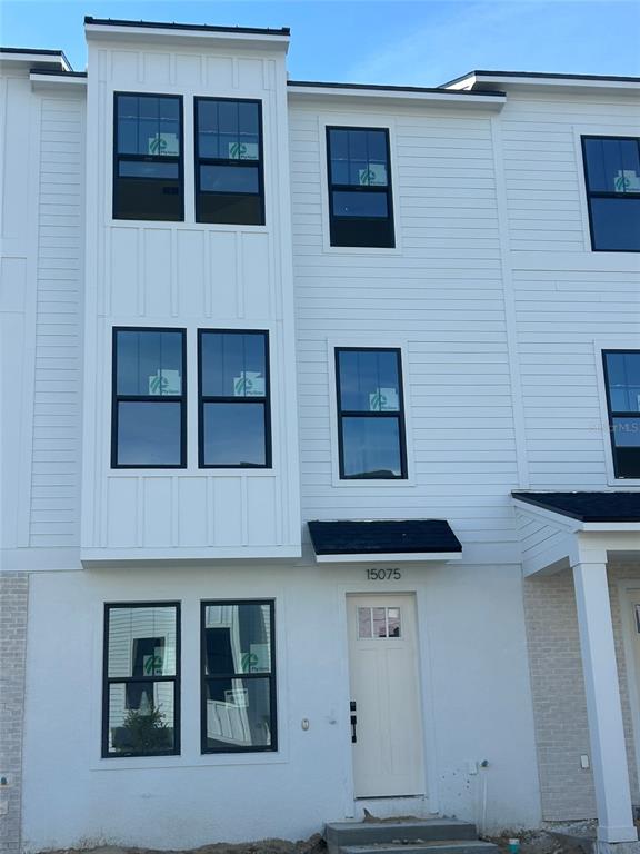 A three-story white townhouse exterior features black-framed windows and a light-colored front door — 15075 GROVESIDE ROAD, WINTER GARDEN, FL