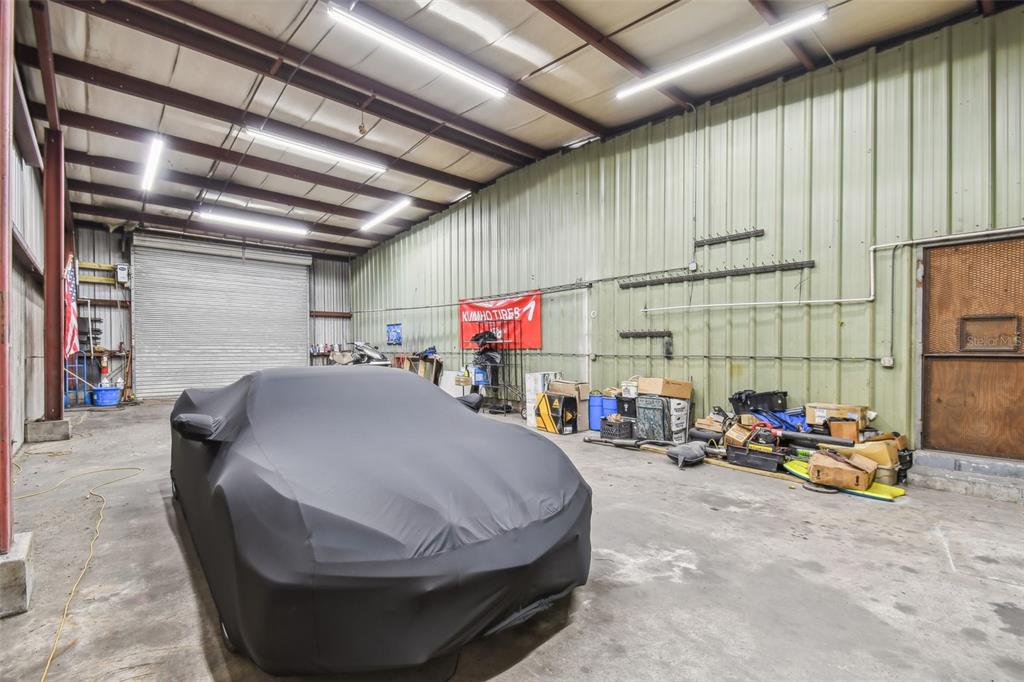 A large, industrial-style garage features a car covered by a tarp and metal wall panels — 304 AVENUE E SW, WINTER HAVEN, FL