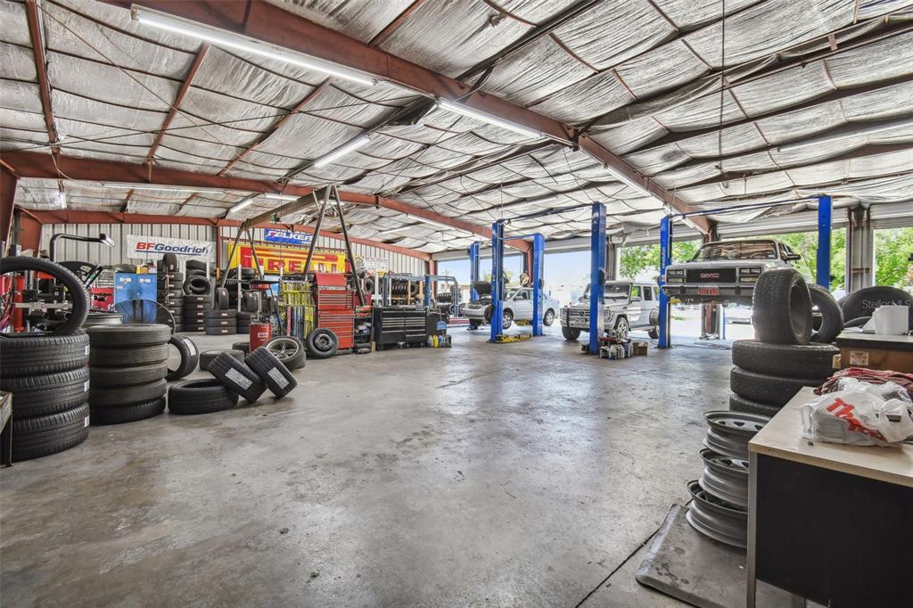 An auto repair shop interior featuring multiple vehicle lifts, stacks of tires, and concrete flooring — 304 AVENUE E SW, WINTER HAVEN, FL