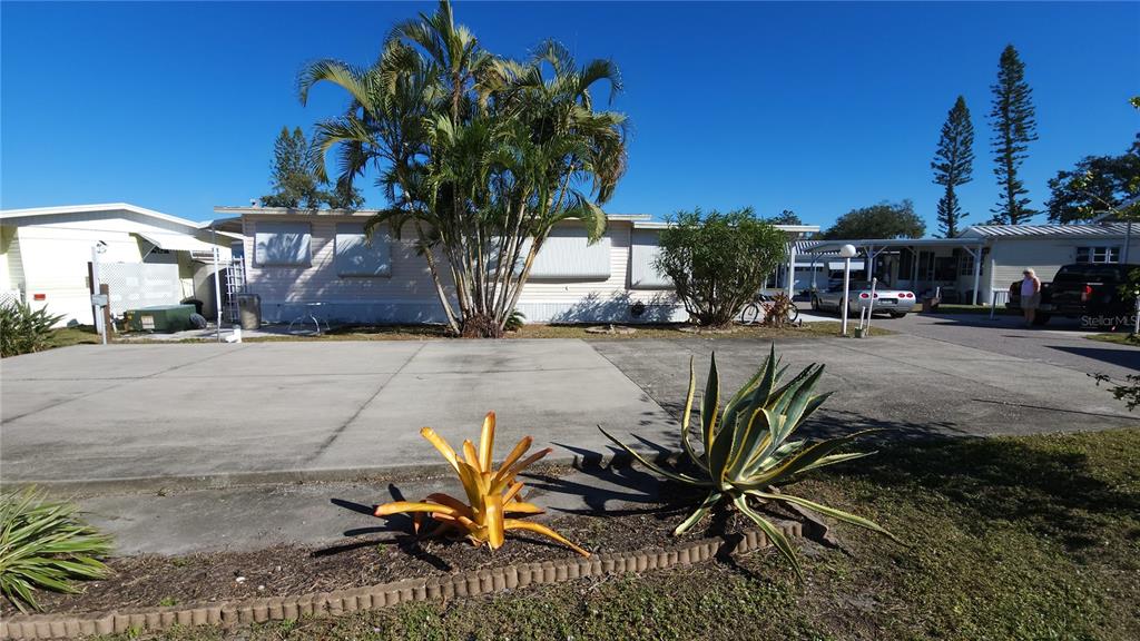 A light-colored mobile home with a concrete driveway, palm tree, and landscaping in front — 3275 26TH AVENUE E UNIT 165, BRADENTON, FL