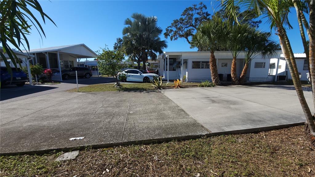 A concrete driveway leads to a white mobile home with palm trees and landscaping — 3275 26TH AVENUE E UNIT 165, BRADENTON, FL