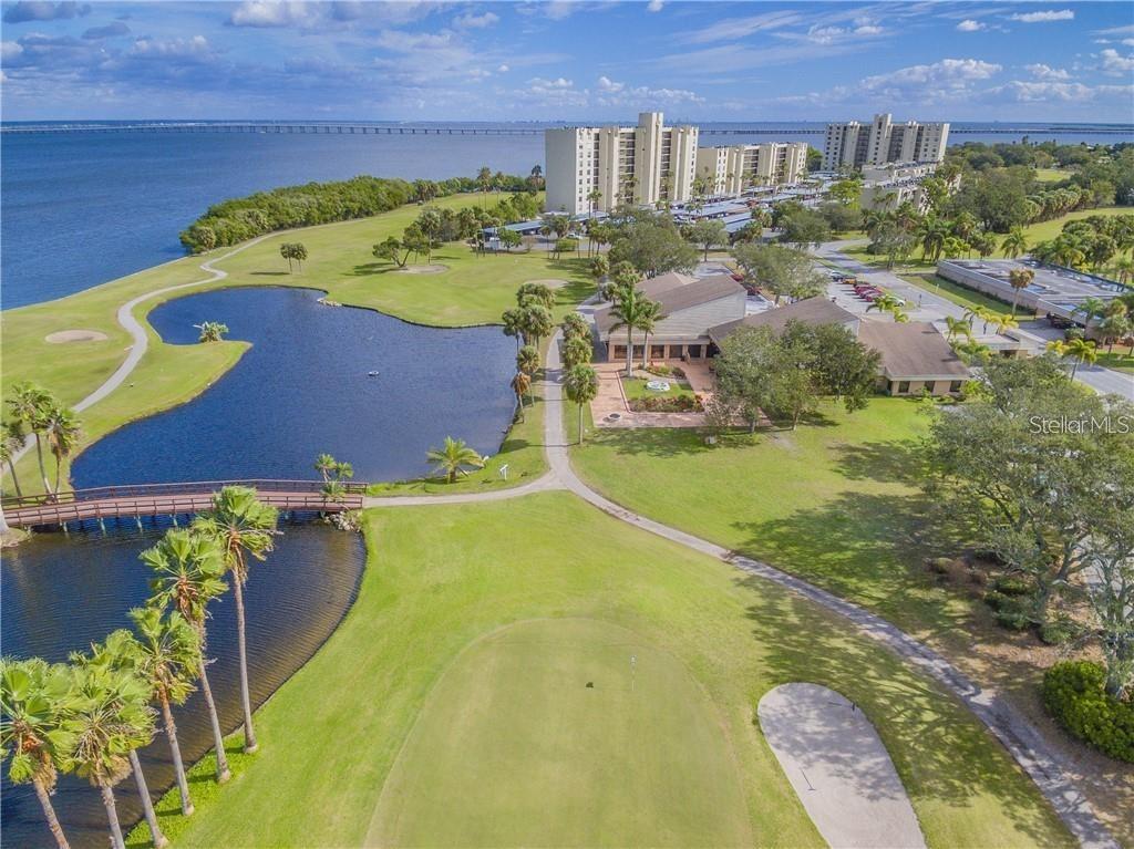 An aerial view of a golf course green, a pond with a bridge, and nearby buildings — 2700 COVE CAY DRIVE UNIT 1-6D, CLEARWATER, FL