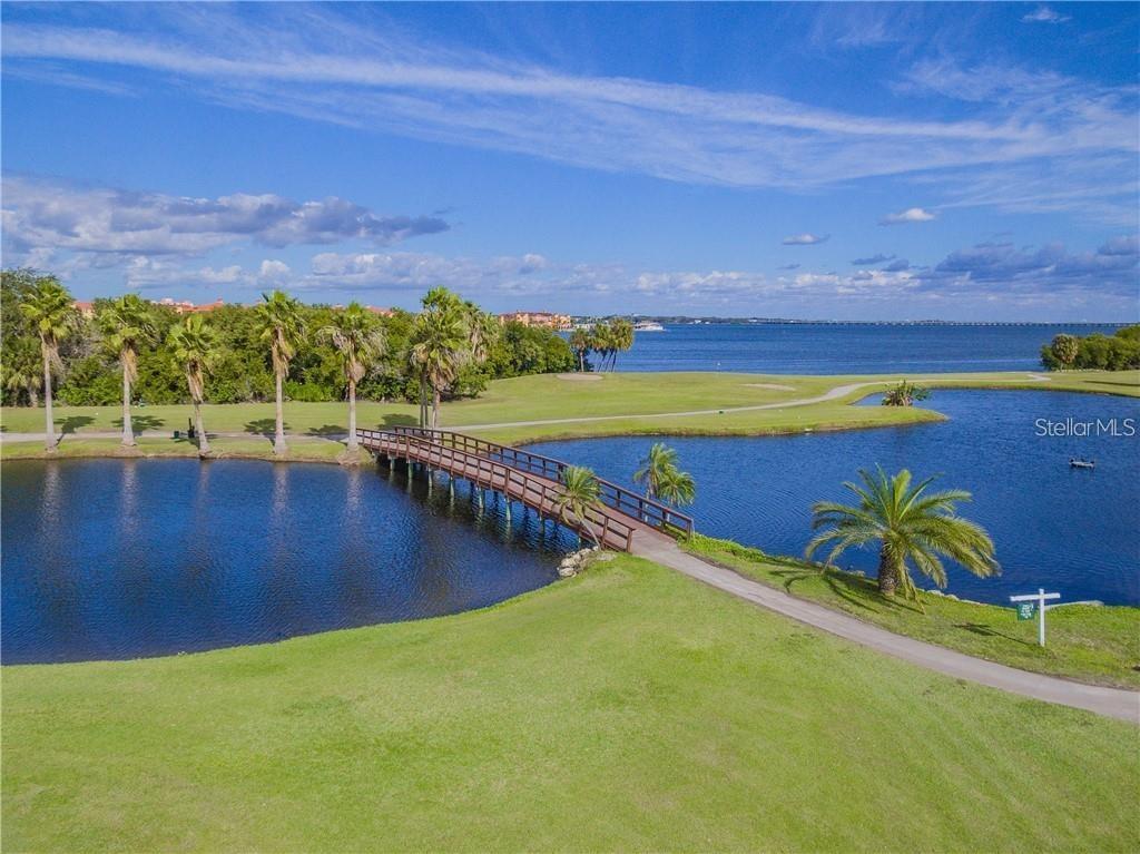 A wooden footbridge crosses a pond on a golf course with a large lake beyond — 2700 COVE CAY DRIVE UNIT 1-6D, CLEARWATER, FL