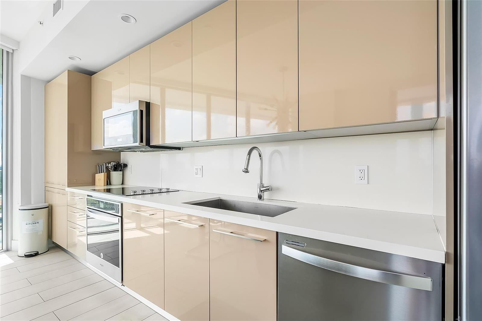 A modern kitchen features glossy beige cabinets, stainless steel appliances, and white countertops — 2000 Metropica Way # 1410, Sunrise FL 33323, SUNRISE, FL