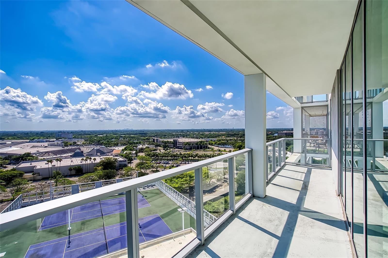 A high-rise balcony overlooks a tennis court and a suburban landscape under a blue sky — 2000 Metropica Way # 1410, Sunrise FL 33323, SUNRISE, FL