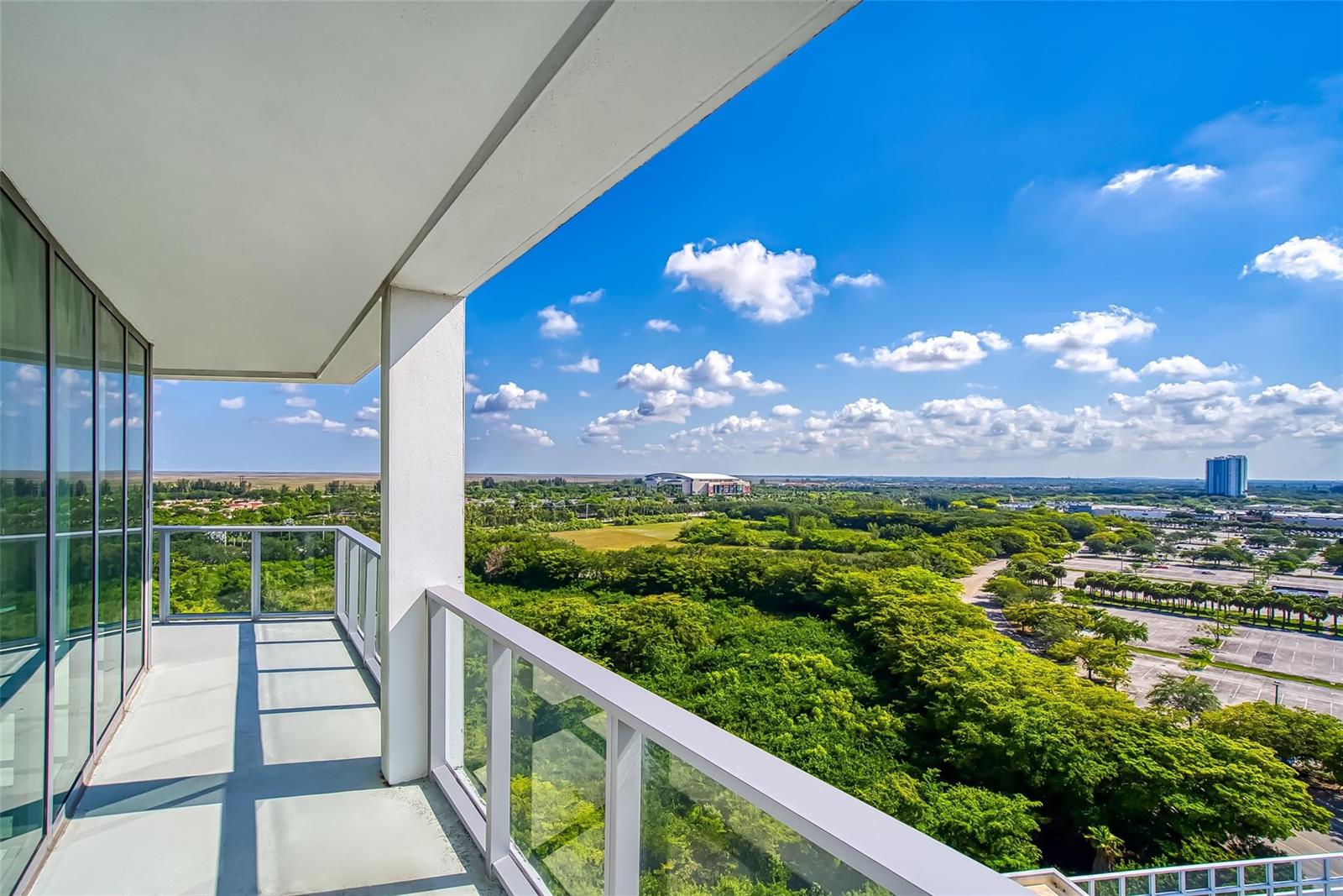 A high-rise balcony overlooks a vast green landscape, a parking lot, and a distant stadium — 2000 Metropica Way # 1410, Sunrise FL 33323, SUNRISE, FL