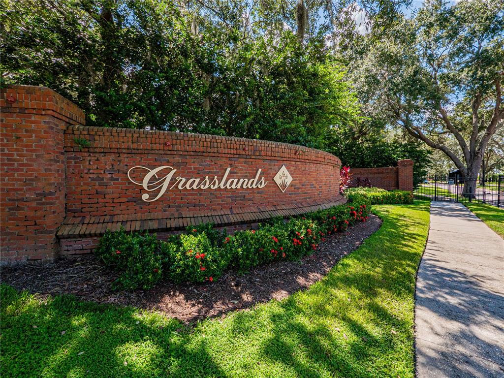 A curved brick wall with the word Grasslands displays the entrance to a residential community — 774 GRASSLANDS VILLAGE CIRCLE UNIT 88, LAKELAND, FL