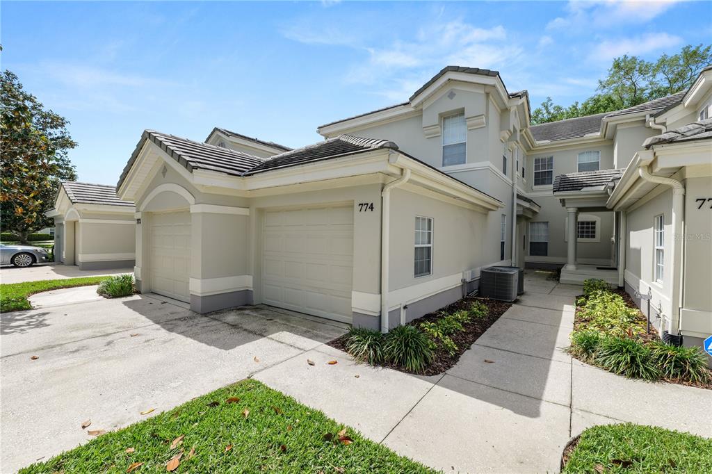 The exterior of a two-story townhouse features a beige stucco facade and a garage — 774 GRASSLANDS VILLAGE CIRCLE UNIT 88, LAKELAND, FL