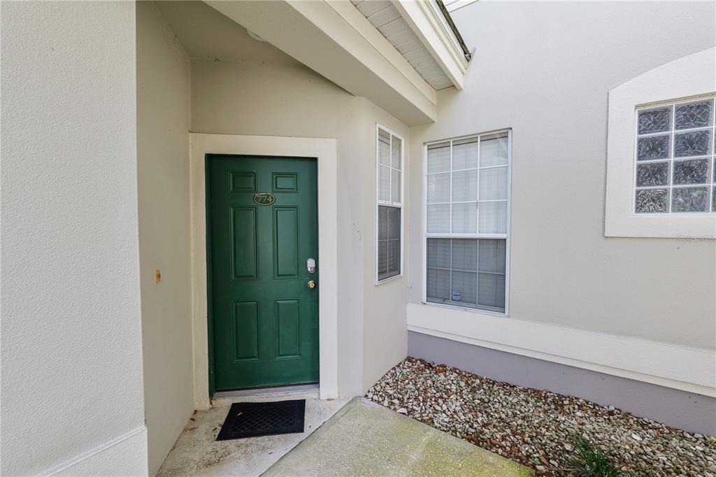 A green front door with the number 774 is set into a beige exterior wall — 774 GRASSLANDS VILLAGE CIRCLE UNIT 88, LAKELAND, FL