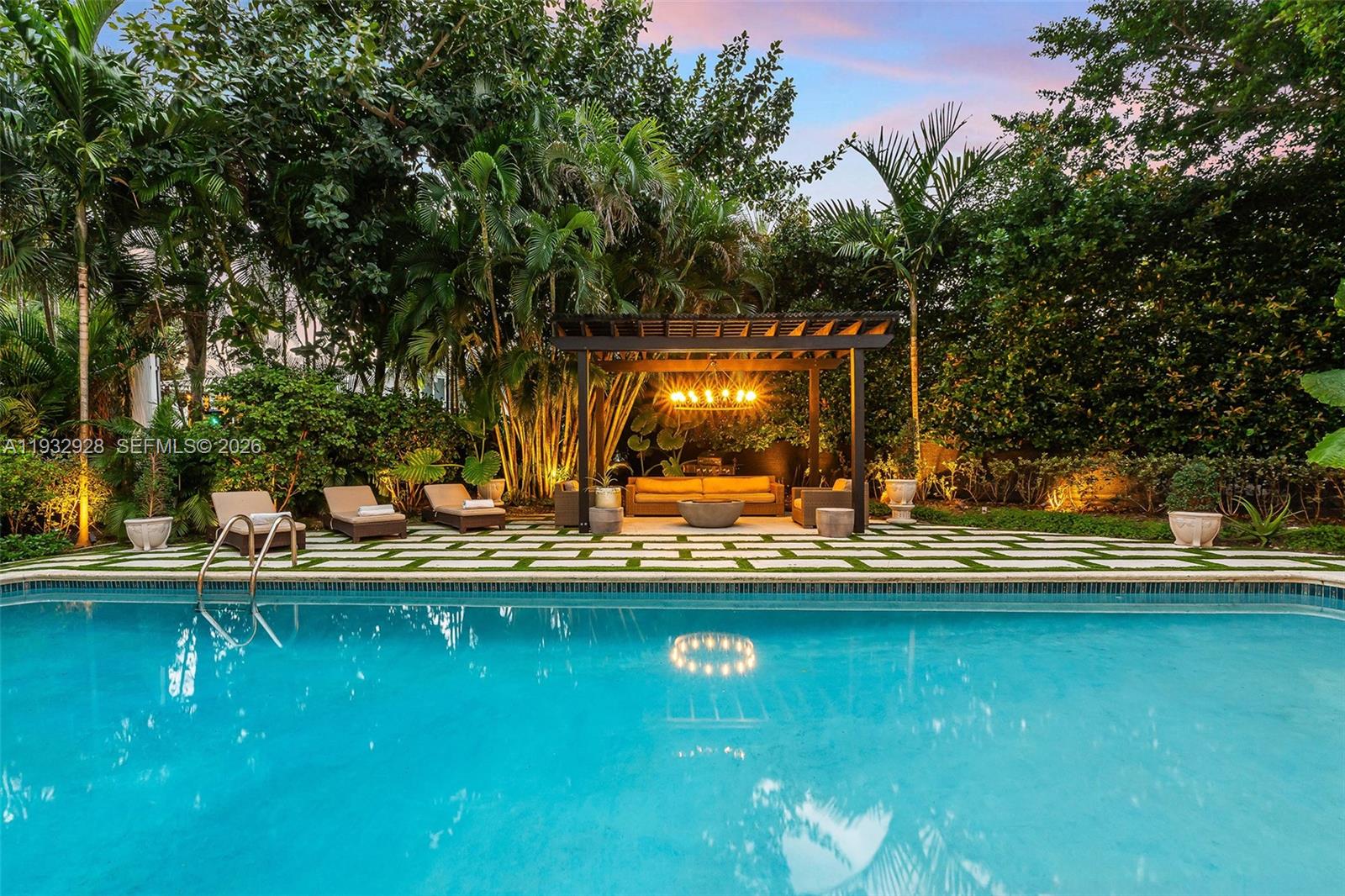 A swimming pool sits in front of a pergola with outdoor seating and lush landscaping — 680 Buttonwood Ln, Miami FL 33137, MIAMI, FL