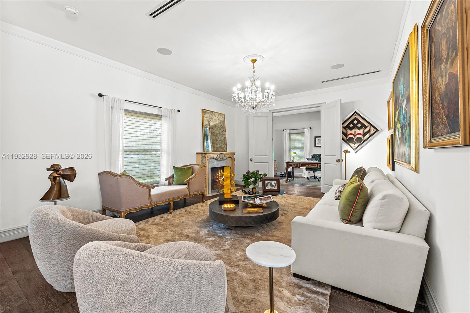 A bright living room features a chandelier, fireplace, white sofa, and two textured armchairs — 680 Buttonwood Ln, Miami FL 33137, MIAMI, FL